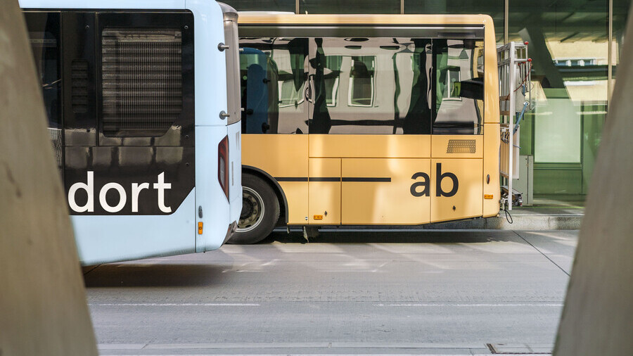 Am Bild sieht man das Hinterteil von zwei Busse - der vordere ist blau und hat die Aufschrift 'dort', der hintere ist orange und hat die Aufschrift 'ab'.